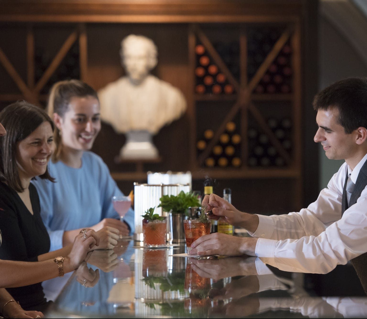 Bartender decorating drinks at bar for two women